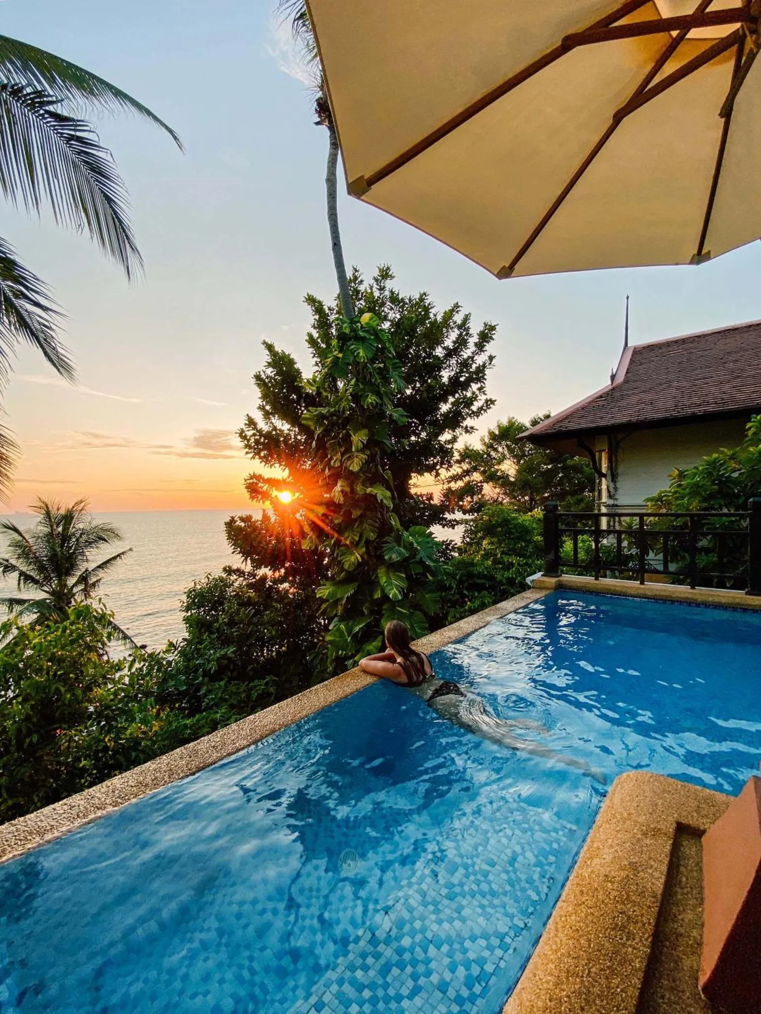 Une personne se détend dans une piscine à débordement face à un coucher de soleil sur l'océan.