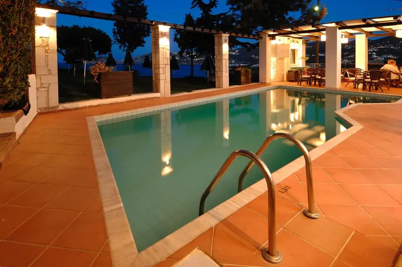 Une piscine rectangulaire éclairée borde une terrasse carrelée avec vue sur la mer.