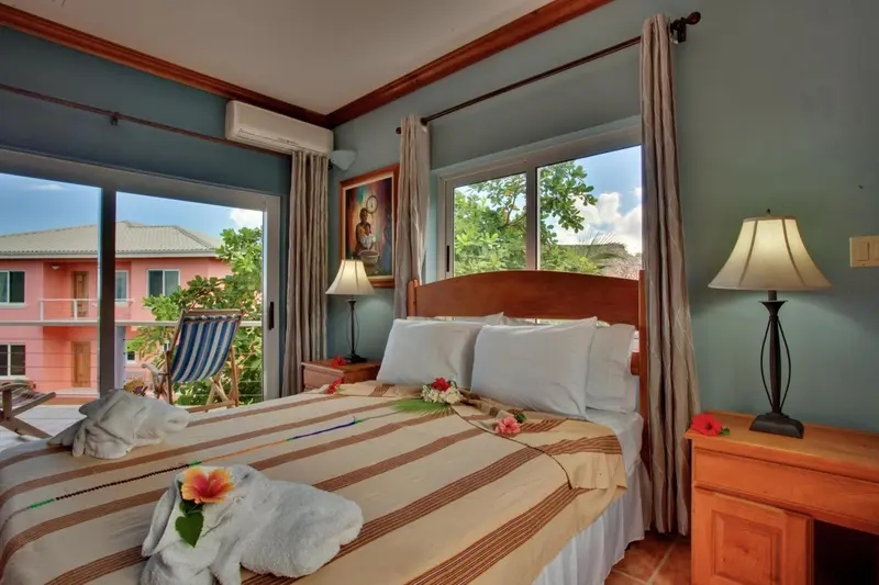 Une chambre lumineuse avec un lit recouvert d'une courtepointe rayée et une vue sur un jardin tropical.
