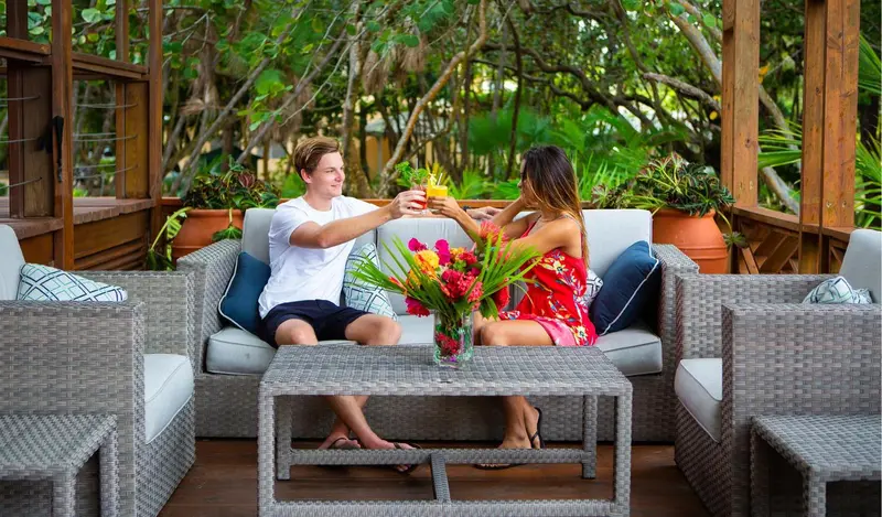Un couple trinque avec des cocktails sur une terrasse aménagée avec des canapés et des plantes.