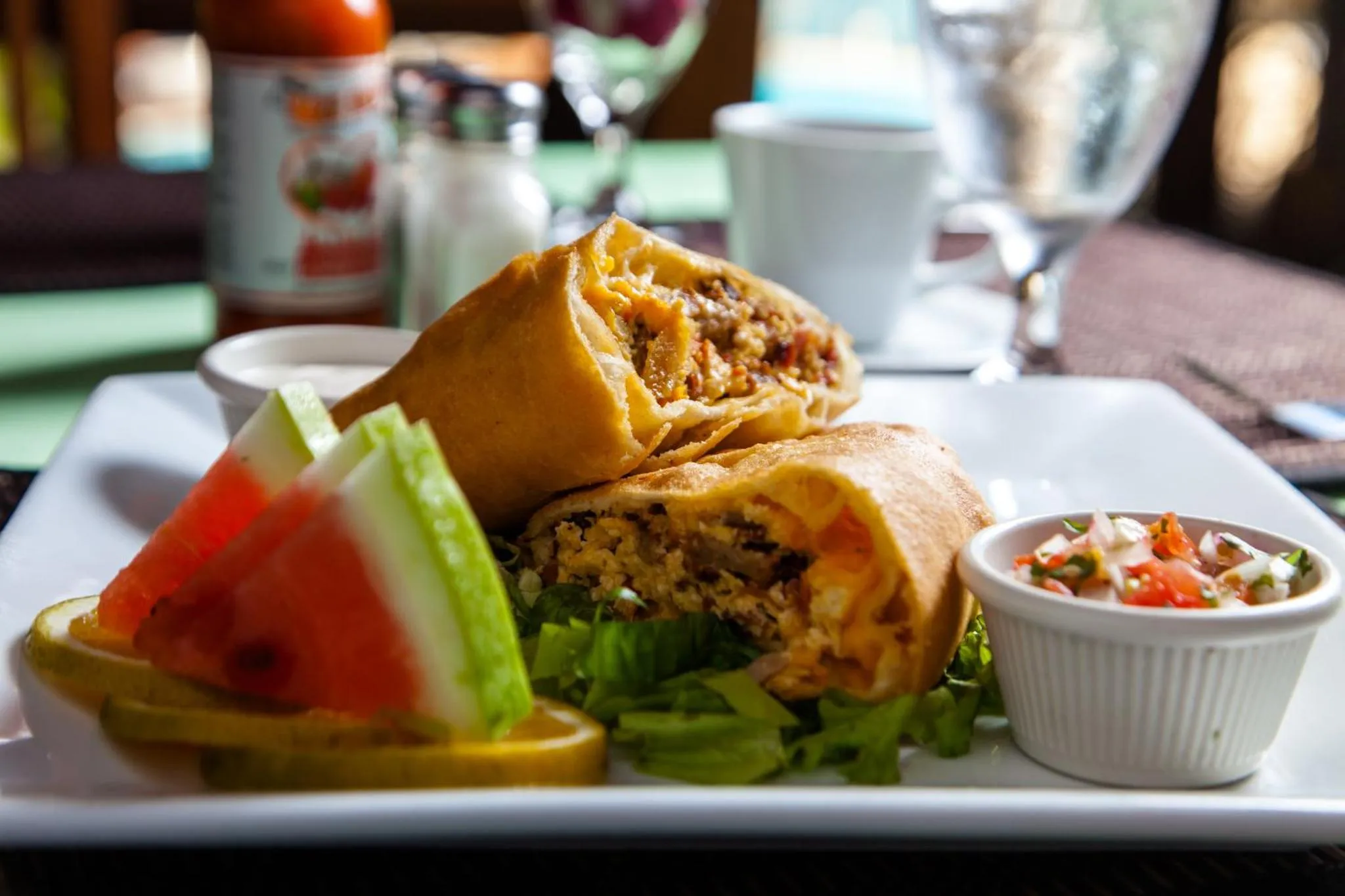 Assiette de nourriture avec un burrito, des tranches de pastèque et une salade.