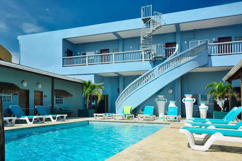 Une piscine turquoise bordée de chaises longues bleues devant un bâtiment bleu clair avec des escaliers.