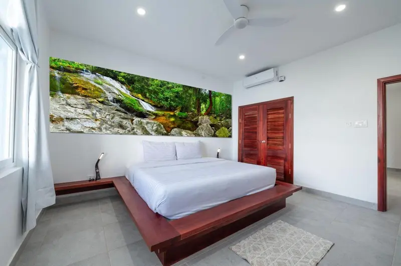 Une chambre lumineuse avec un grand lit et une décoration murale représentant une cascade.