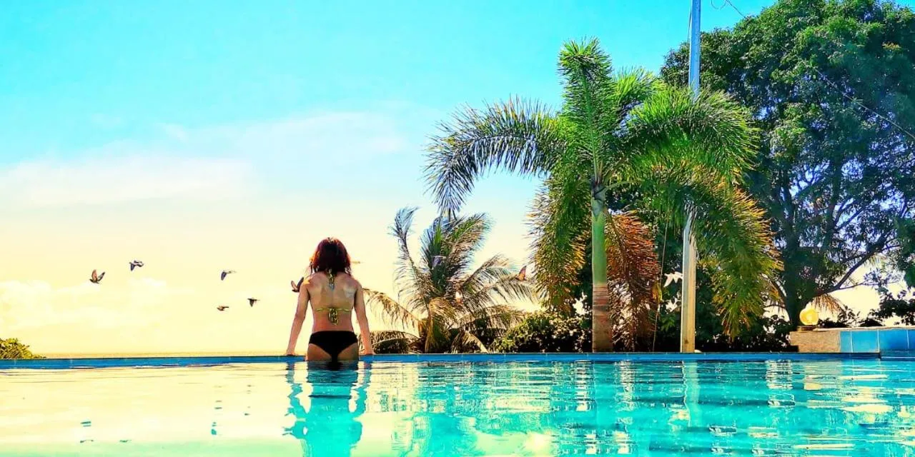 Une personne se tient au bord d'une piscine face à la mer et à la végétation tropicale.