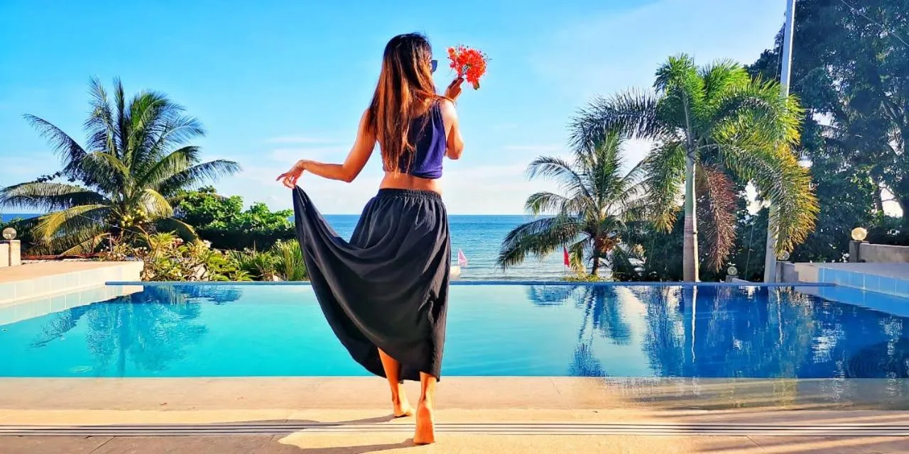 Une femme se tient dos à la caméra, près d'une piscine à débordement avec vue sur la mer.