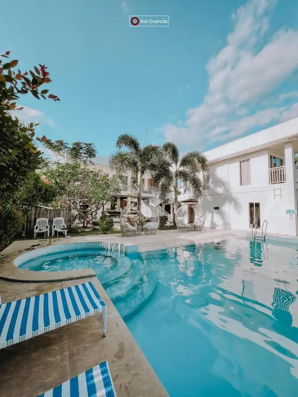 Piscine rectangulaire entourée d'une terrasse avec des transats et des palmiers sous un ciel bleu.