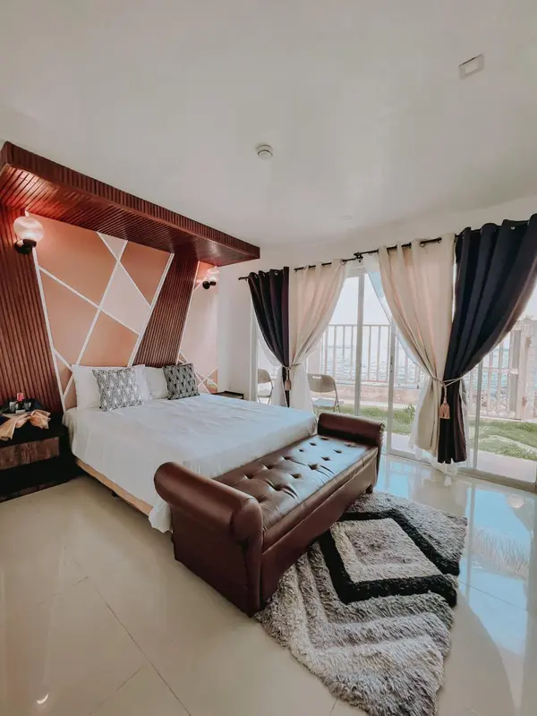 Une chambre lumineuse avec un grand lit et un banc au pied du lit.