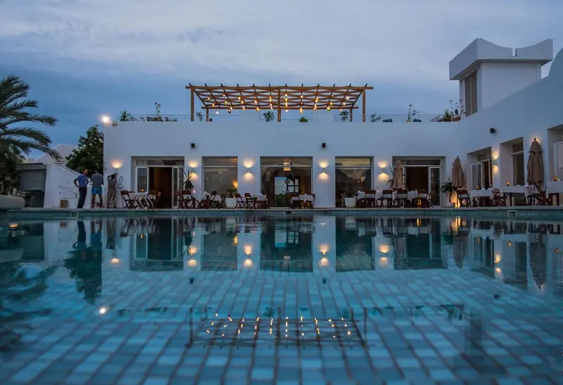 Une piscine reflète les lumières d'un bâtiment blanc et d'une pergola éclairée.