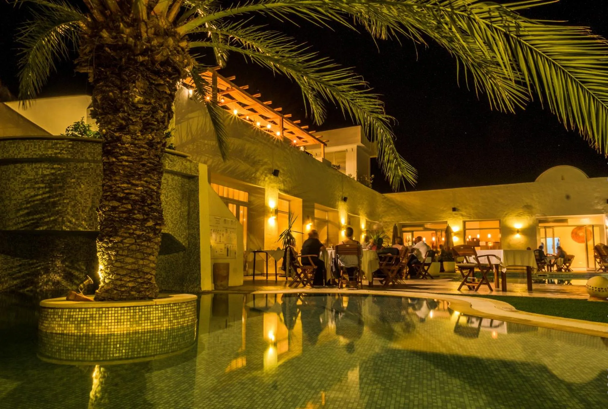 Terrasse illuminée avec tables et chaises près d'une piscine.