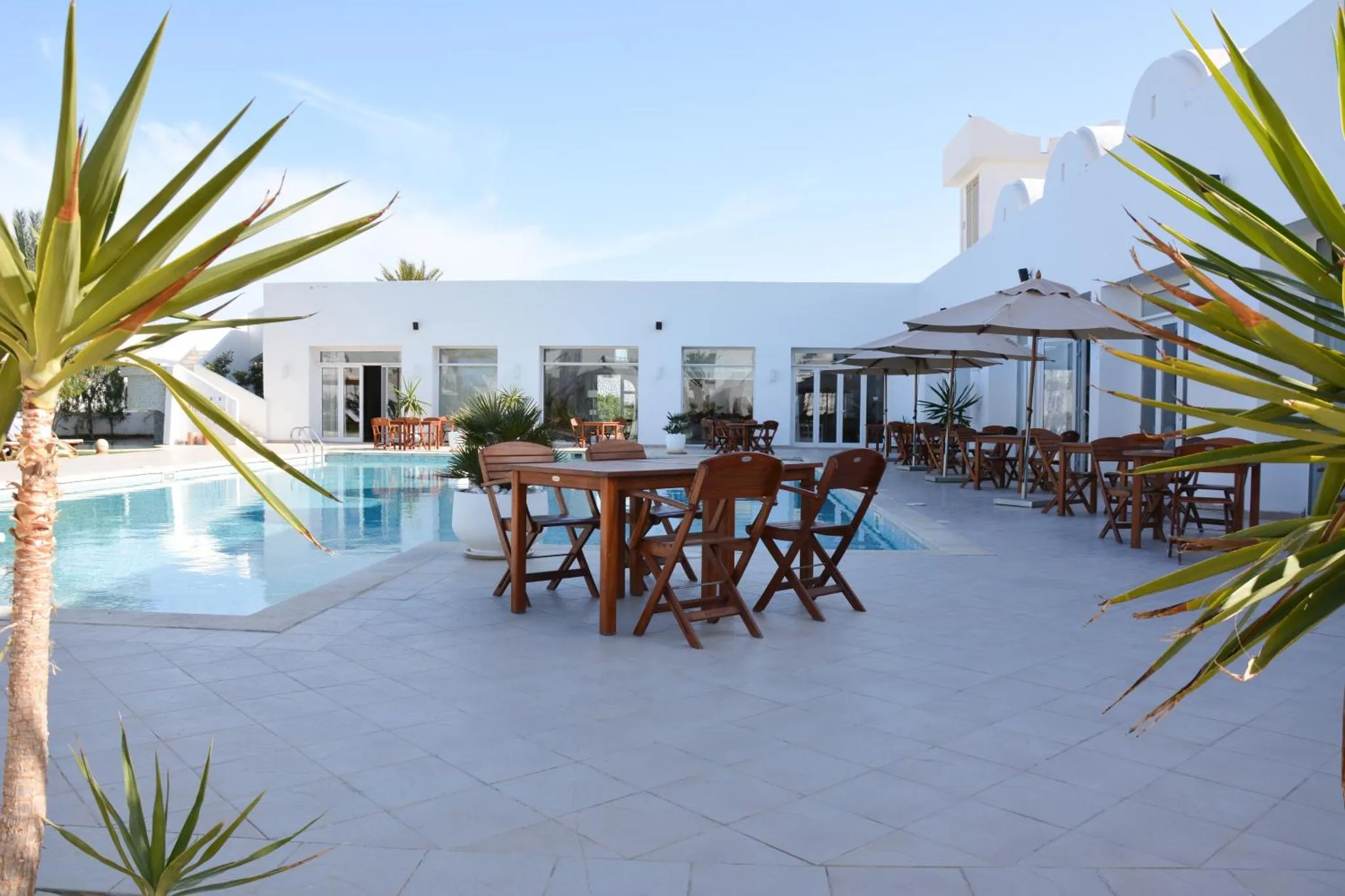 Terrasse avec tables et parasols près d'une piscine ensoleillée.