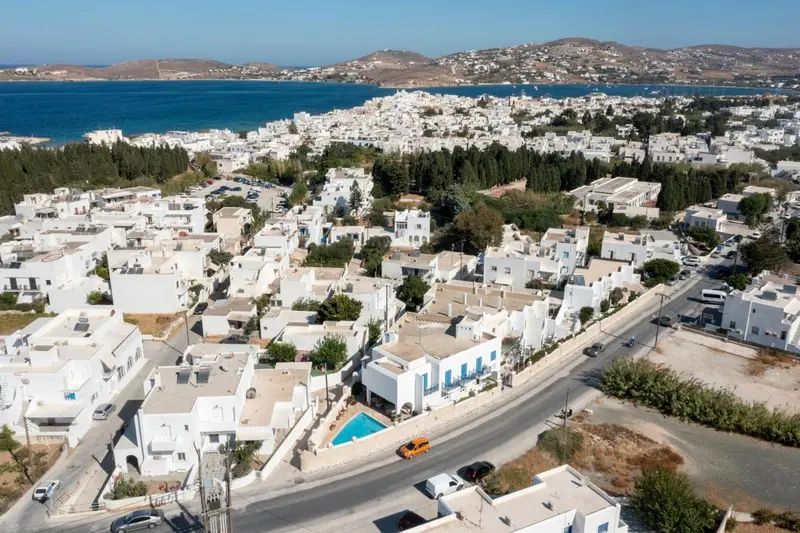 Vue aérienne d'un village blanc avec des bâtiments aux toits plats et une piscine turquoise.
