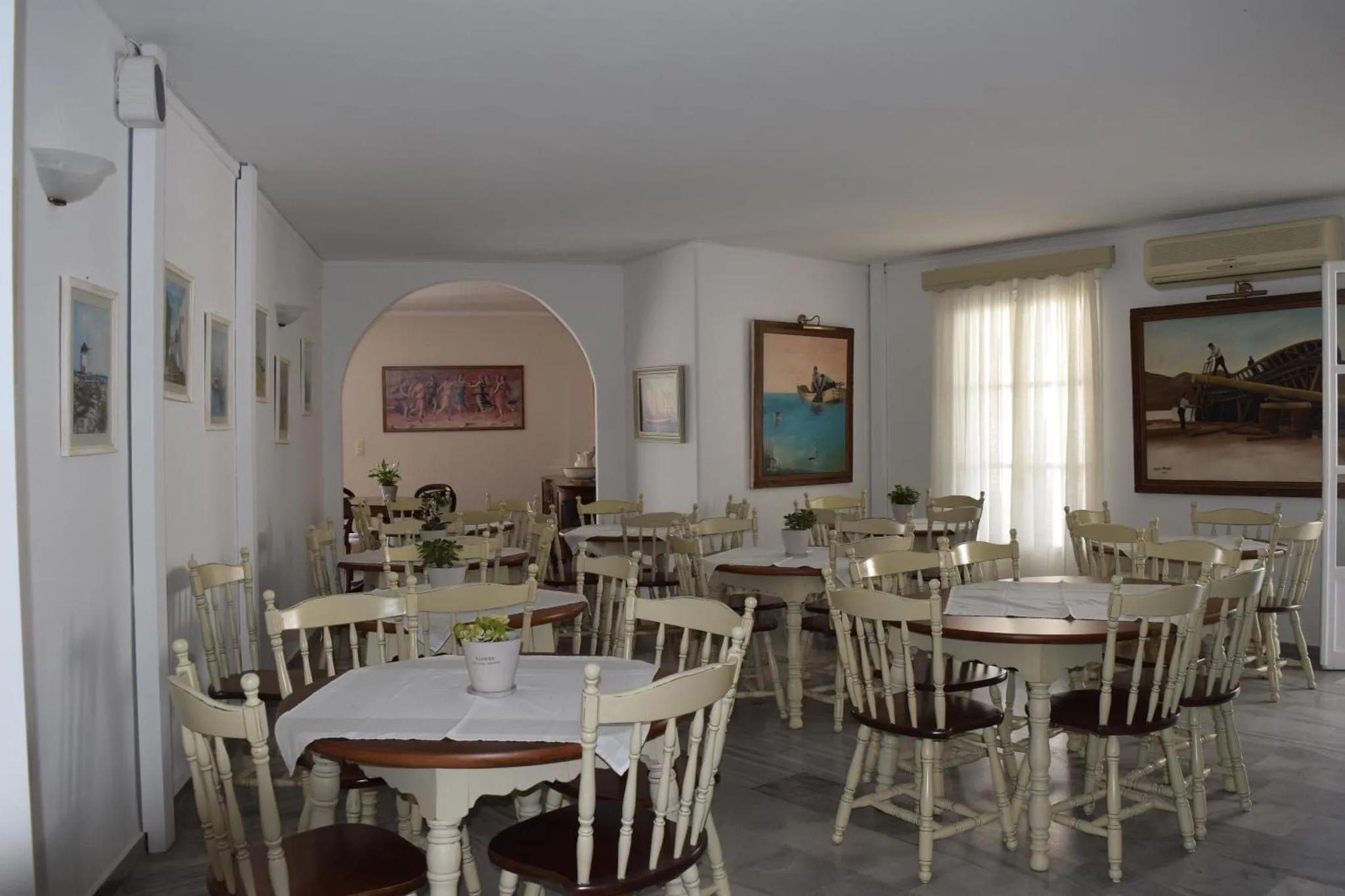 Une salle lumineuse avec des tables et des chaises blanches est décorée de tableaux.