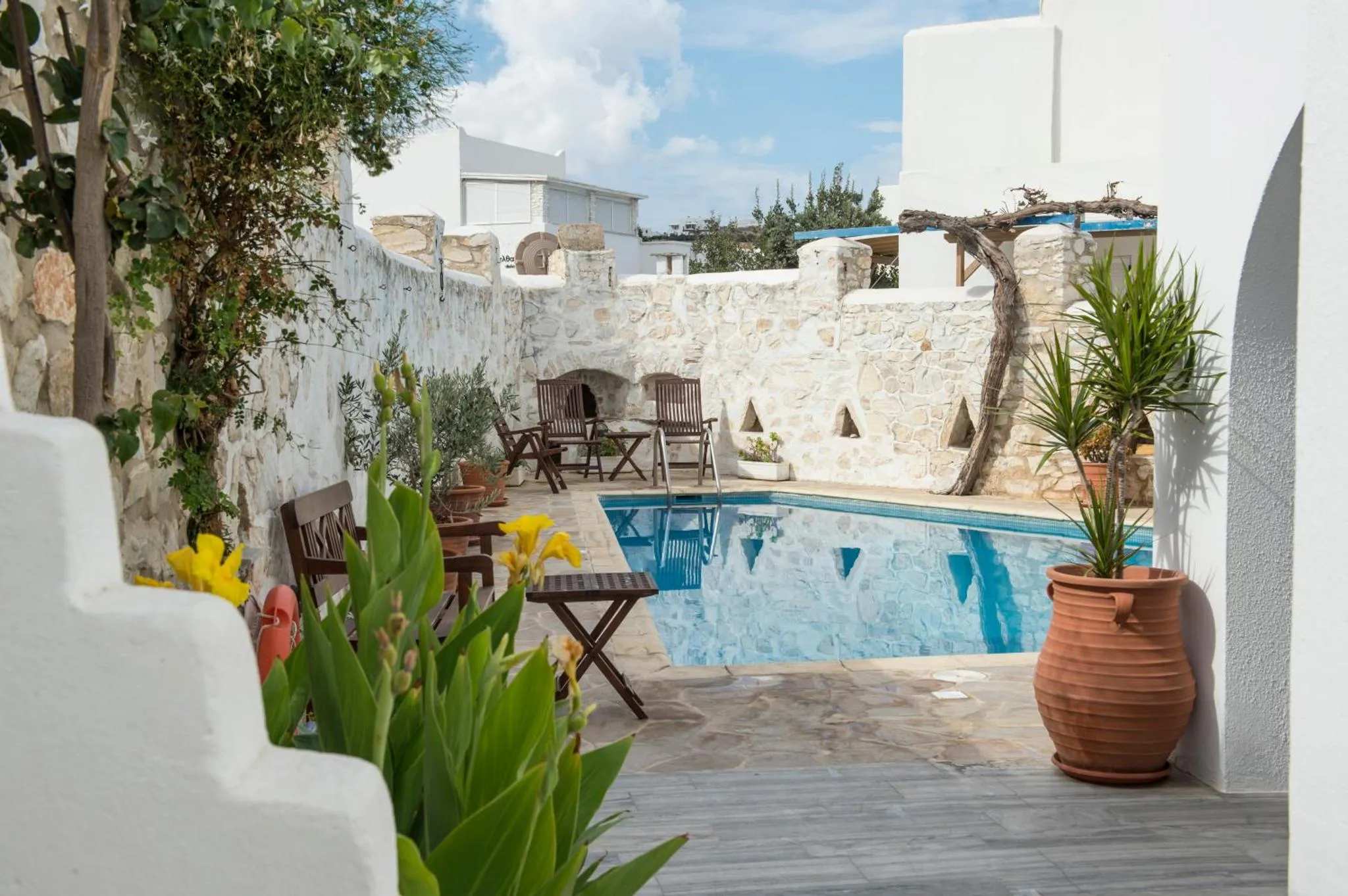 Une petite piscine rectangulaire est entourée d'une terrasse aménagée avec des chaises et des plantes.