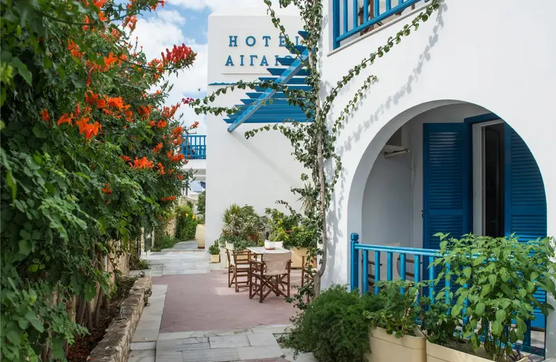 Façade blanche d'un bâtiment ornée de fleurs et d'une arche bleue, avec une table et des chaises sur une terrasse.