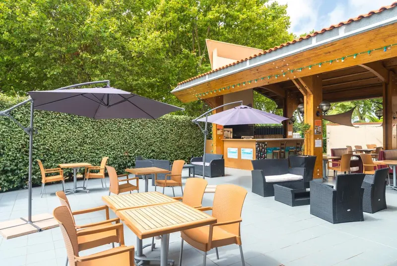 Terrasse ombragée avec tables et chaises près d'un bar extérieur.