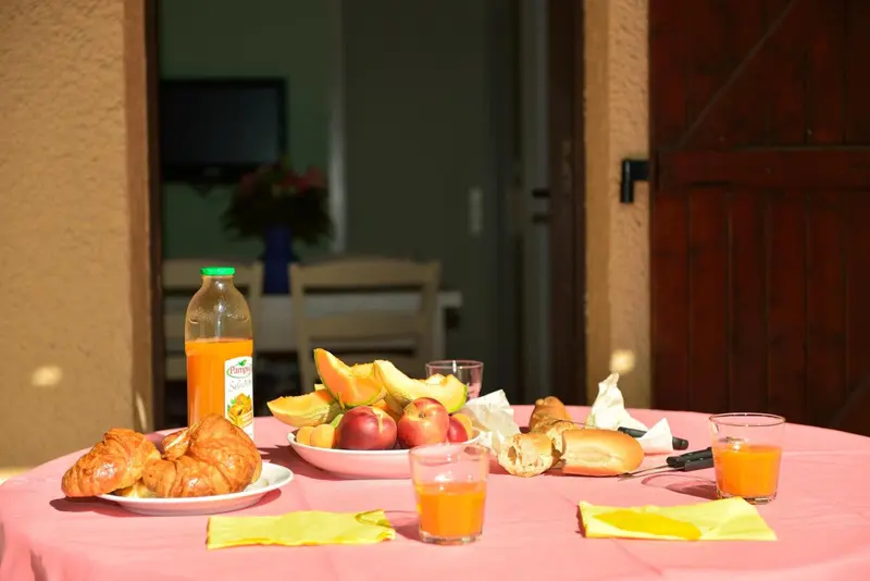Une table ronde est dressée avec un petit déjeuner composé de viennoiseries, de fruits et de jus d'orange.
