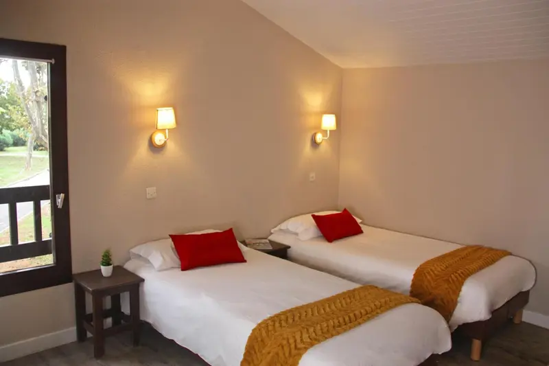 Une chambre lumineuse avec deux lits simples et des oreillers rouges.