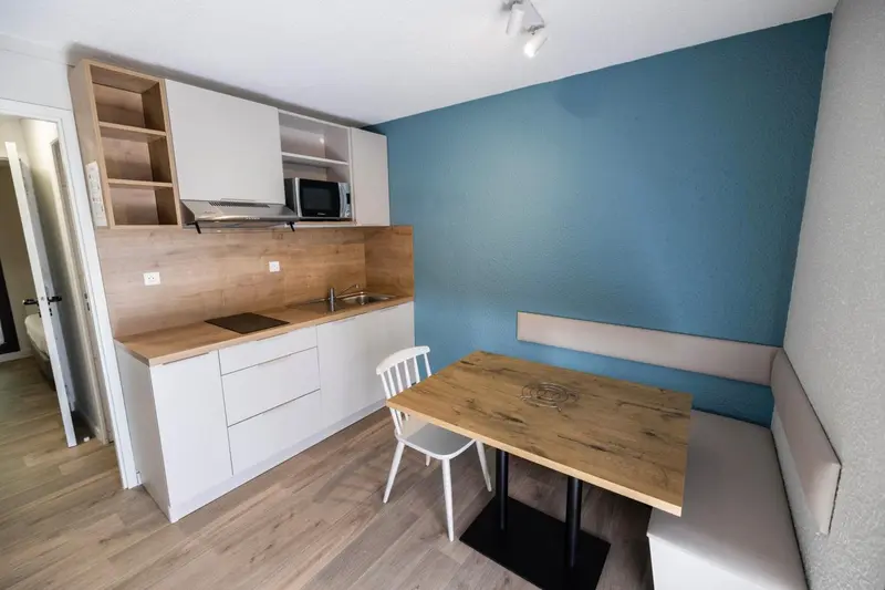 Une kitchenette moderne s'ouvre sur un coin repas avec une table et une banquette.