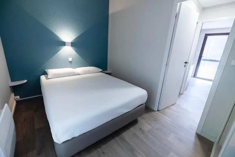 Une chambre lumineuse avec un lit double et un mur bleu.