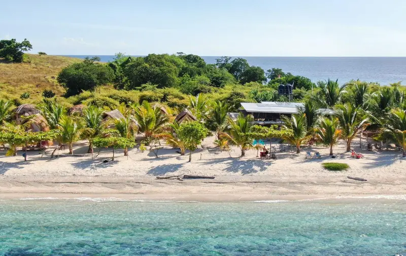 Vue aérienne d'un complexe de bungalows sur une plage de sable blanc bordée de palmiers.