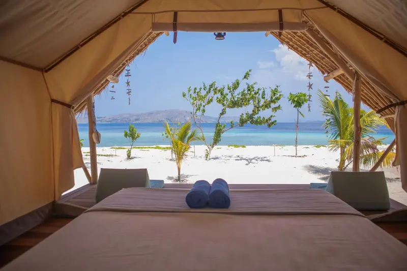 Vue sur une plage de sable blanc et la mer depuis l'intérieur d'une tente.