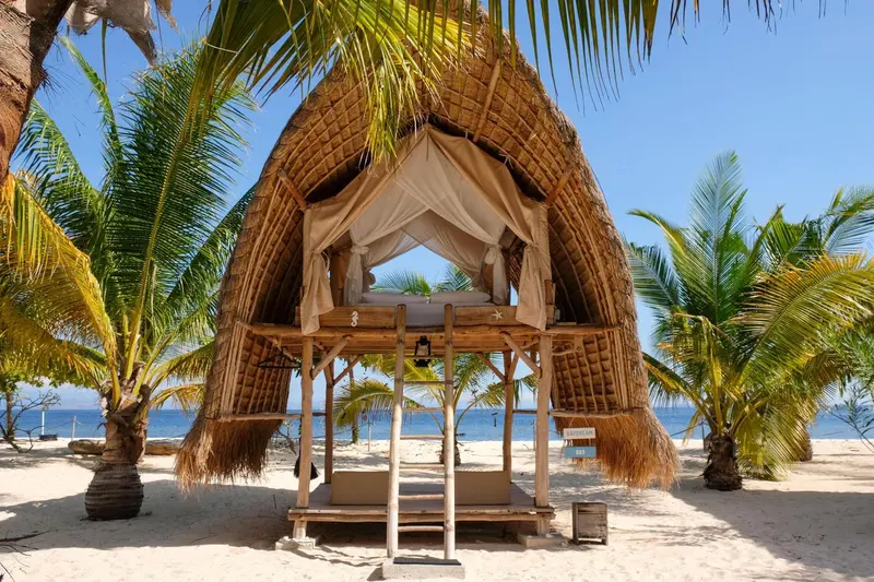 Cabane de plage traditionnelle avec toit de chaume et moustiquaire.