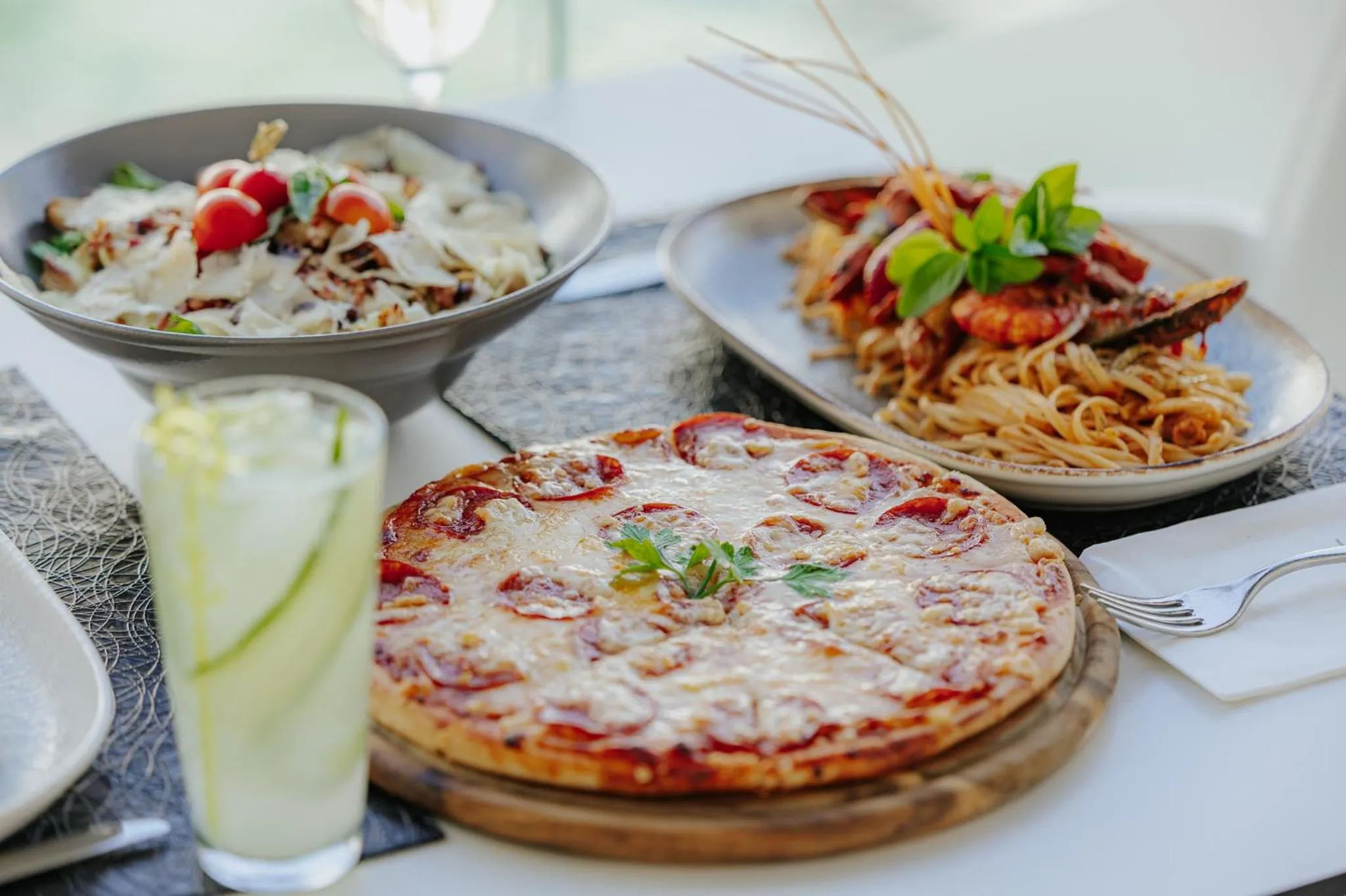 Assiettes de pâtes, pizza et boisson fraîche sur une table.