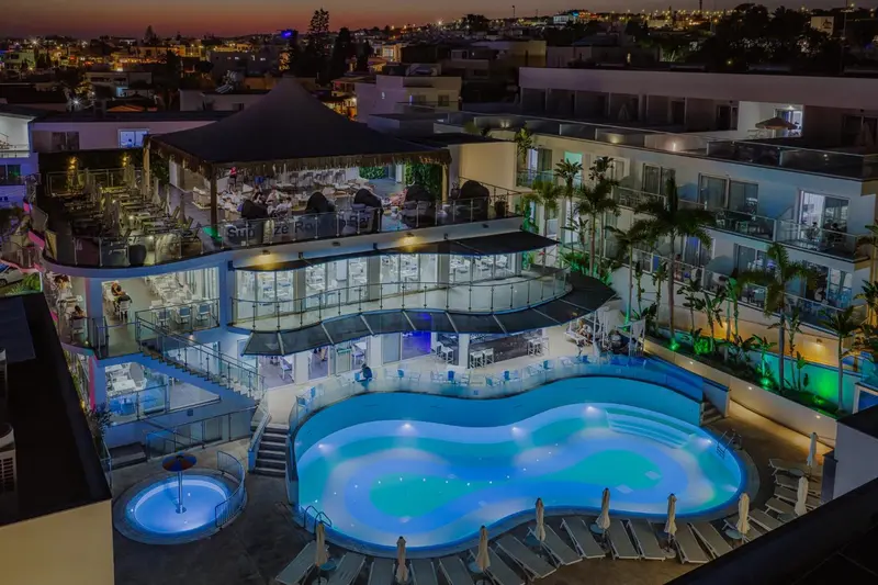 Vue aérienne d'un complexe hôtelier illuminé avec une piscine et des palmiers.