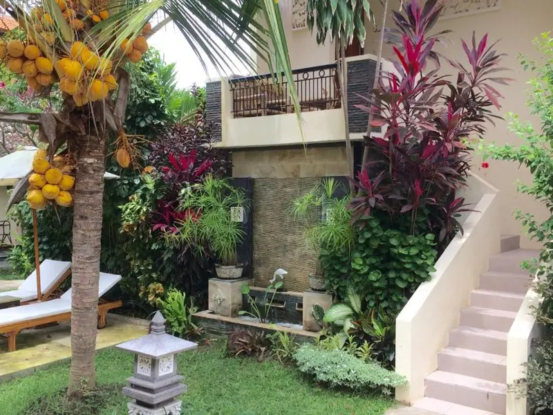 Jardin tropical avec fontaine et escalier menant à une terrasse.