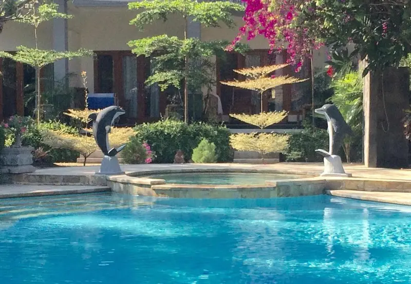 Piscine turquoise entourée de végétation luxuriante et de sculptures de dauphins.