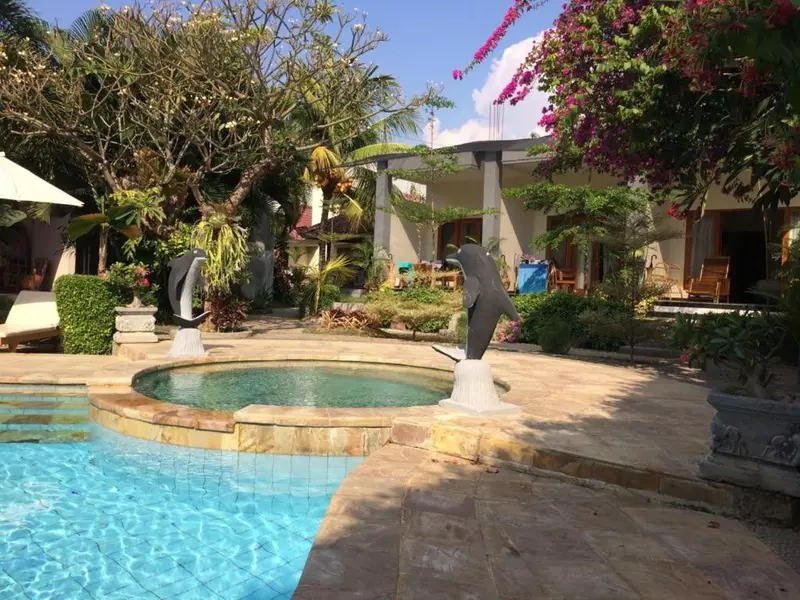 Une piscine turquoise bordée d'une terrasse en pierre, avec des statues de dauphins et une végétation luxuriante.