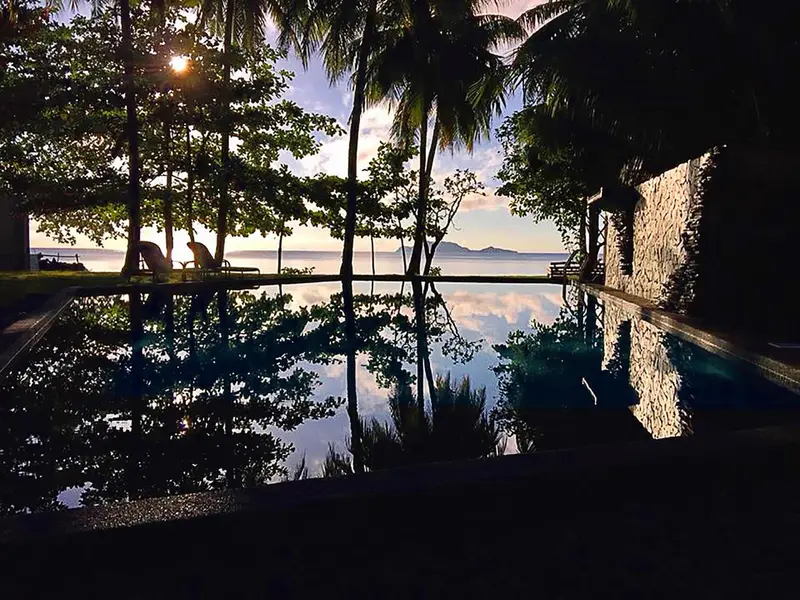 Une piscine à débordement reflète le ciel et la végétation tropicale.