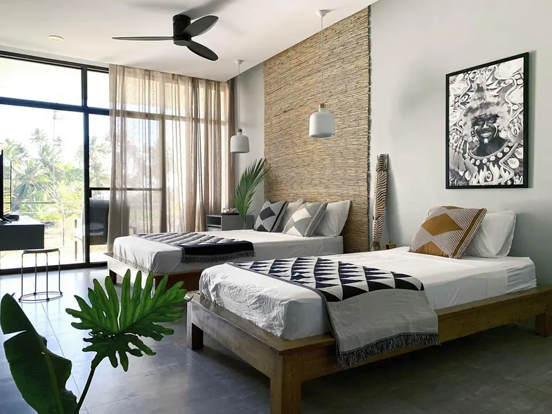 Chambre lumineuse avec deux lits simples et décoration tropicale.
