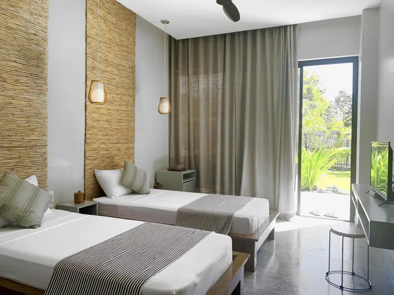 Chambre lumineuse avec deux lits simples et un accès à l'extérieur.