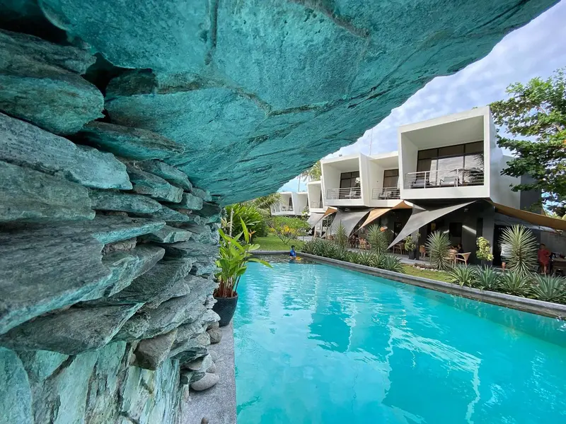 Une piscine turquoise s'étend devant un bâtiment moderne et une végétation luxuriante.