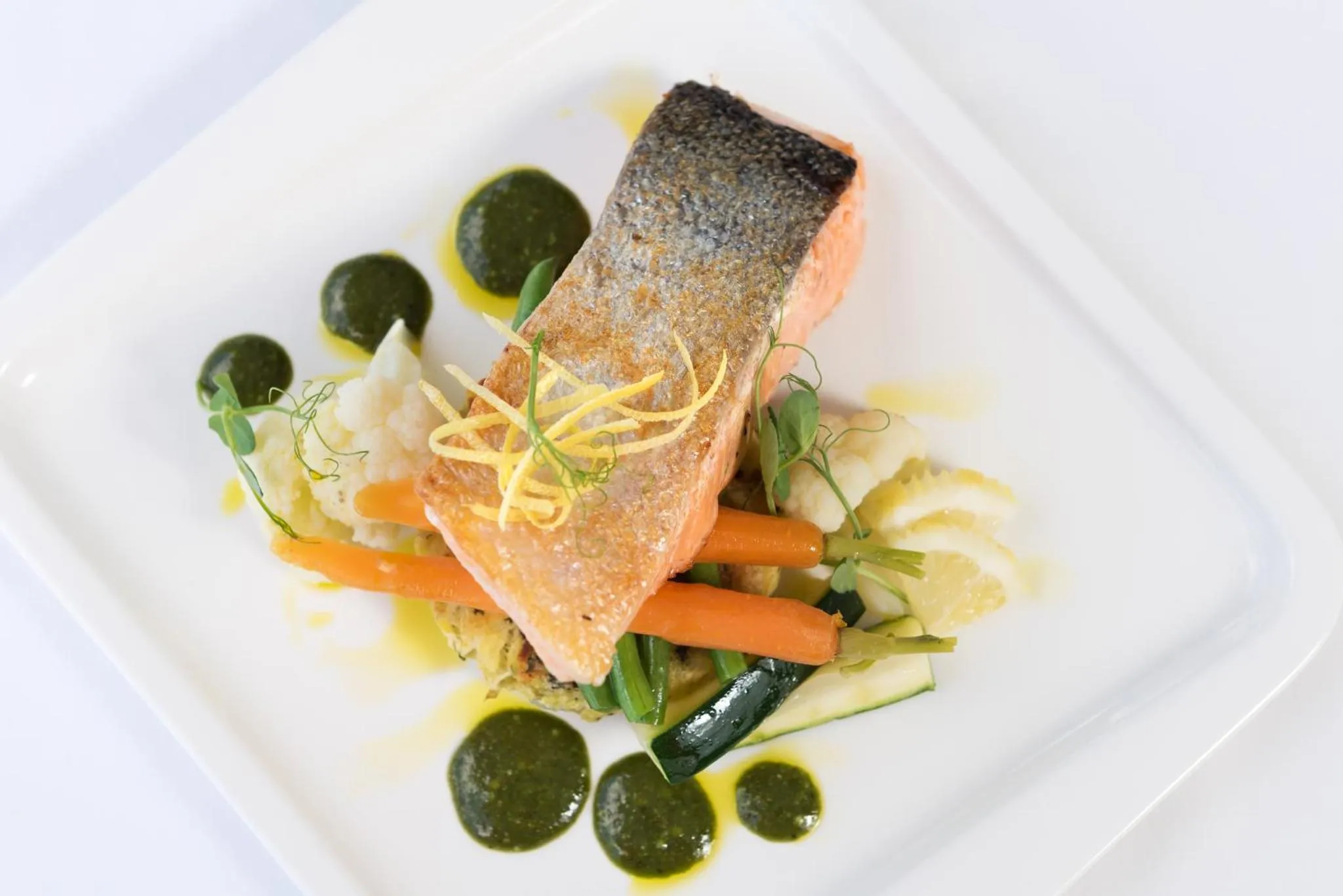 Un plat de saumon grillé est présenté avec des légumes et une sauce verte.
