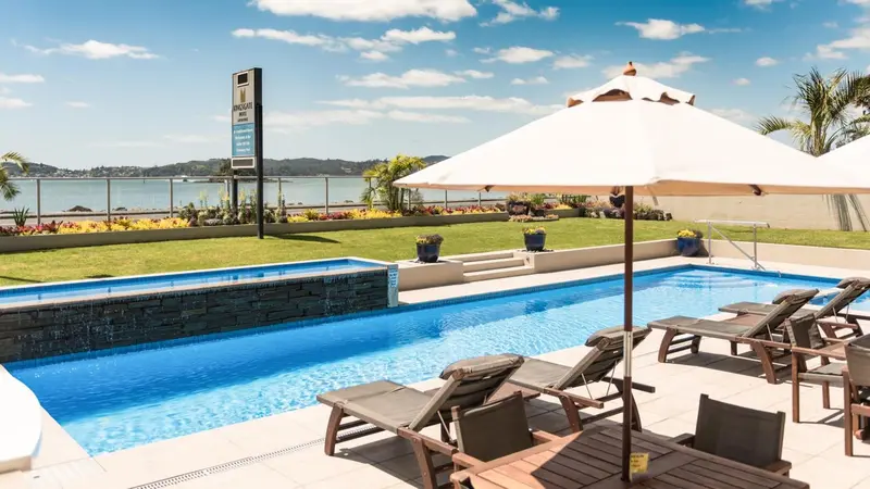 Transats et parasols bordent une piscine rectangulaire avec un mur de pierres.