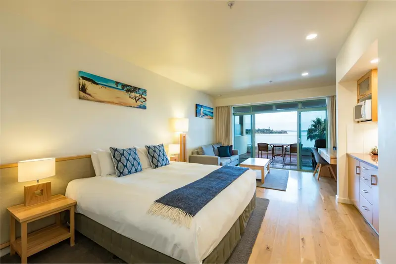 Une chambre lumineuse avec un grand lit et un coin salon donnant sur une terrasse.