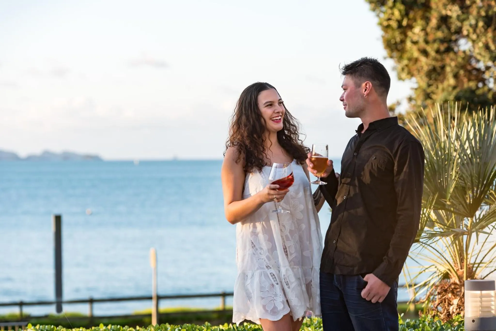Un couple souriant déguste des boissons en bord de mer.