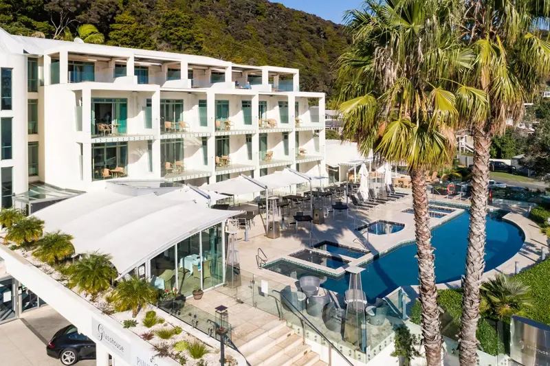 Vue aérienne d'un bâtiment blanc avec des balcons donnant sur une piscine et une végétation luxuriante.