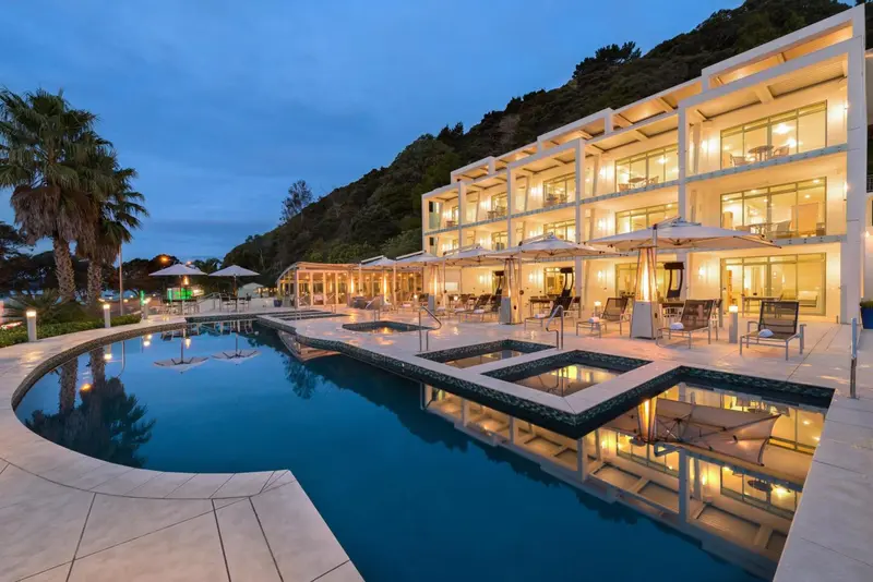 Bâtiment blanc moderne avec piscine et végétation luxuriante au crépuscule.