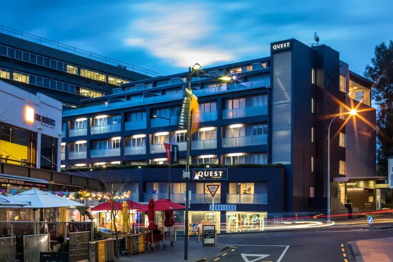 Façade d'un bâtiment moderne avec des fenêtres éclairées et un panneau indiquant un nom.