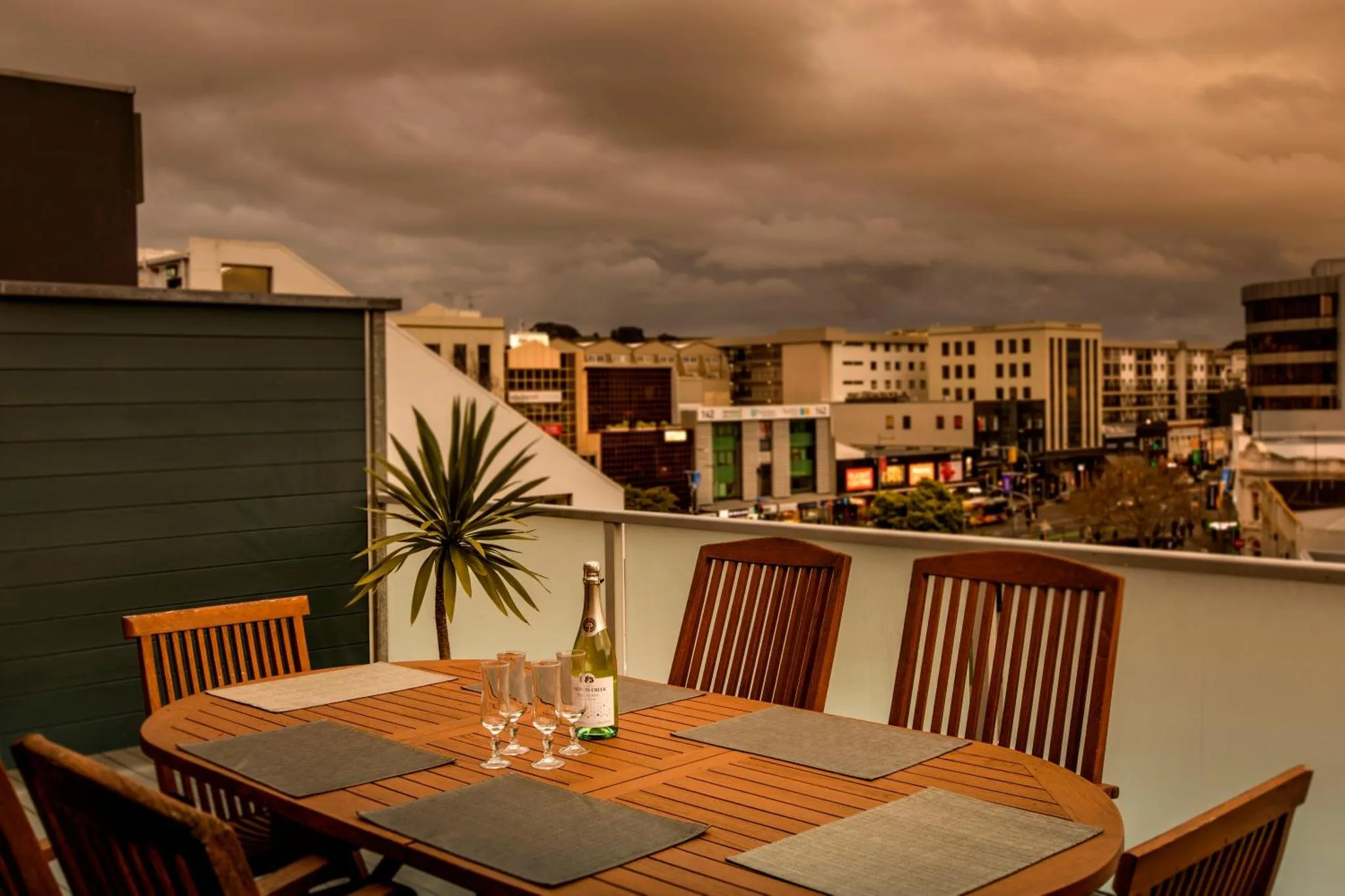 Table et chaises en bois sur une terrasse avec vue sur la ville au crépuscule.