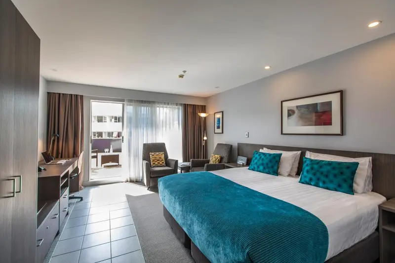 Une chambre lumineuse avec un grand lit et un coin salon donnant sur une terrasse.