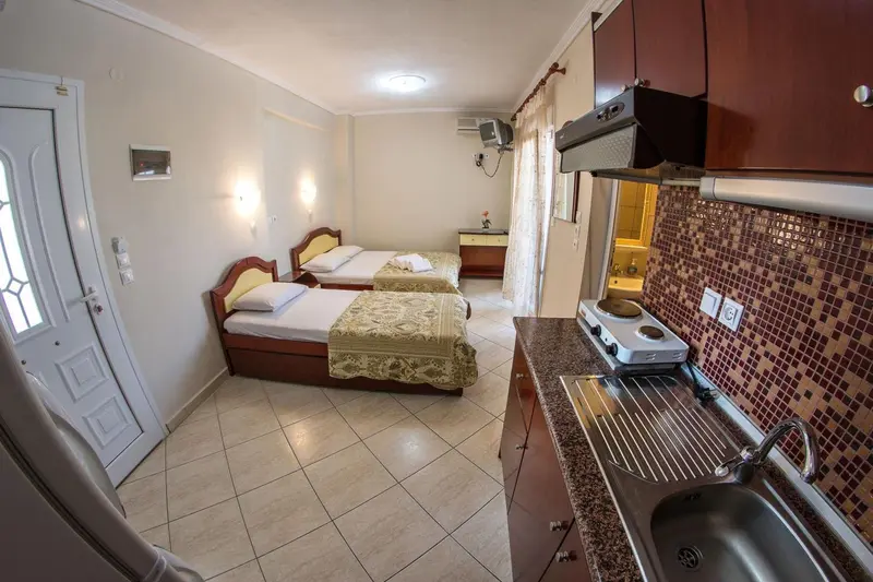 Une chambre lumineuse avec un coin cuisine et deux lits simples.