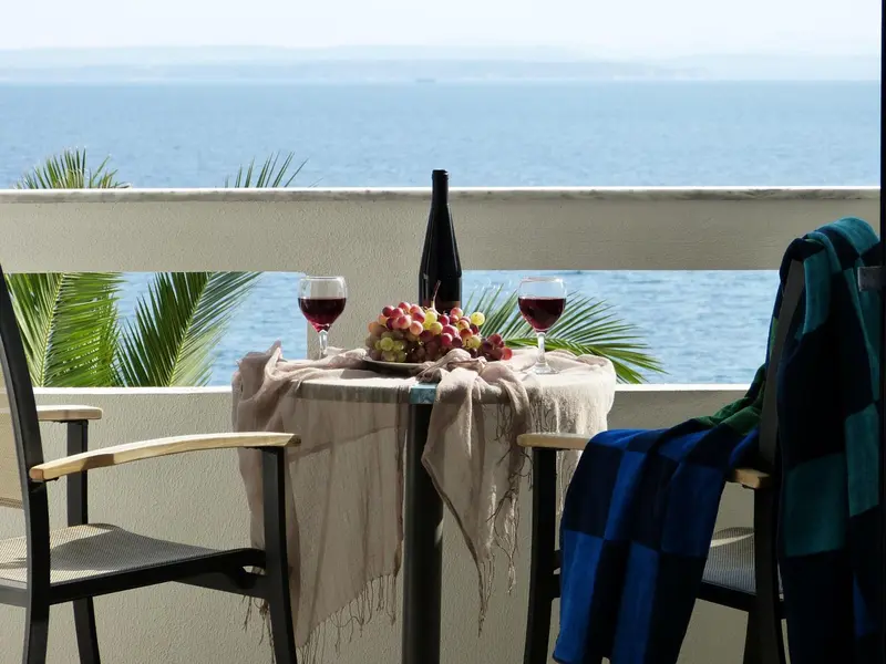Une table avec des verres de vin et des fruits est mise en scène sur une terrasse avec vue sur la mer.