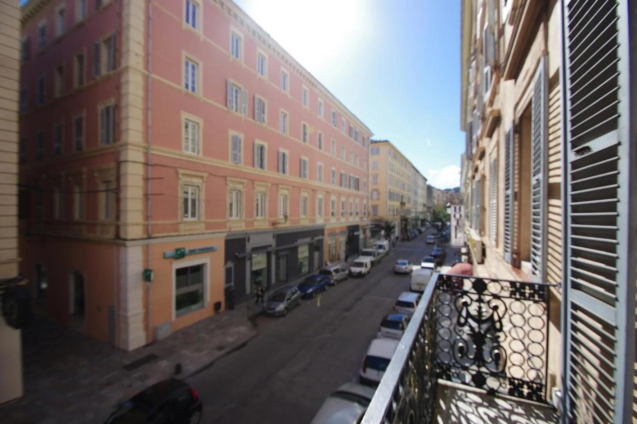 Vue sur une rue bordée d'immeubles et de voitures depuis un balcon.