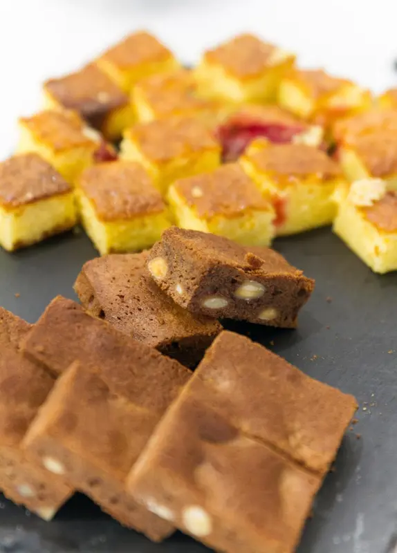 Assortiment de petits gâteaux et de brownies présentés sur une ardoise.