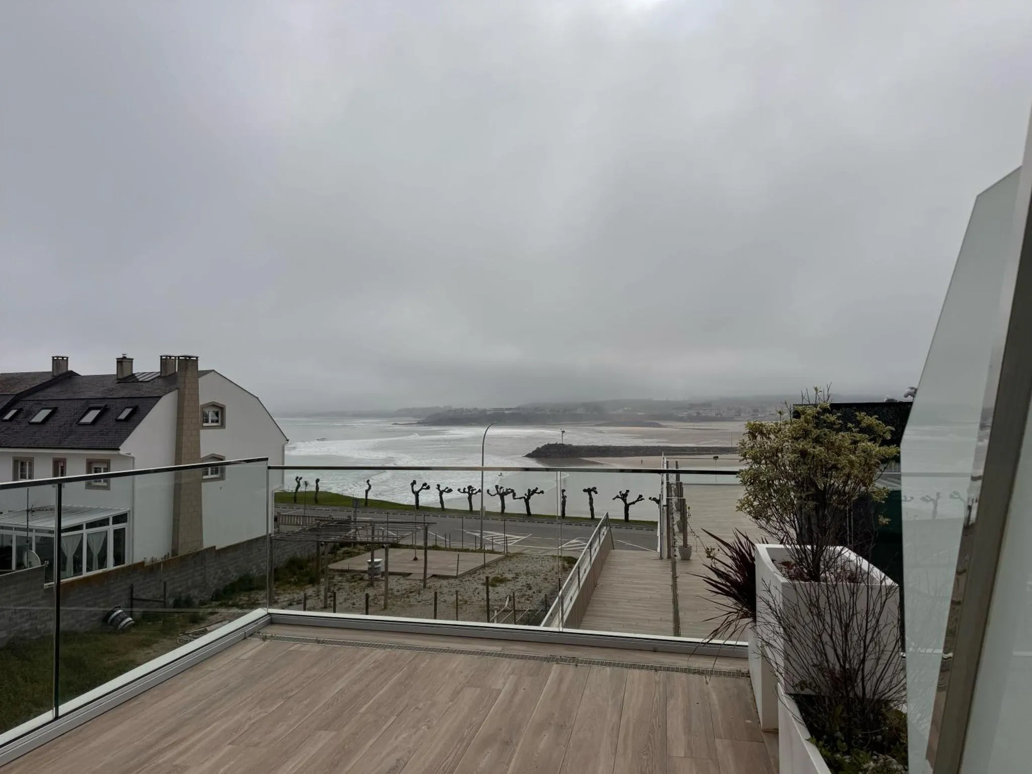 Terrasse en bois avec vue sur la mer et les bâtiments environnants sous un ciel nuageux.
