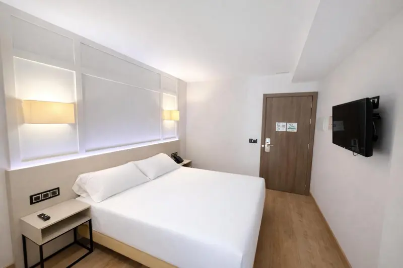 Chambre lumineuse avec un grand lit et une télévision murale.